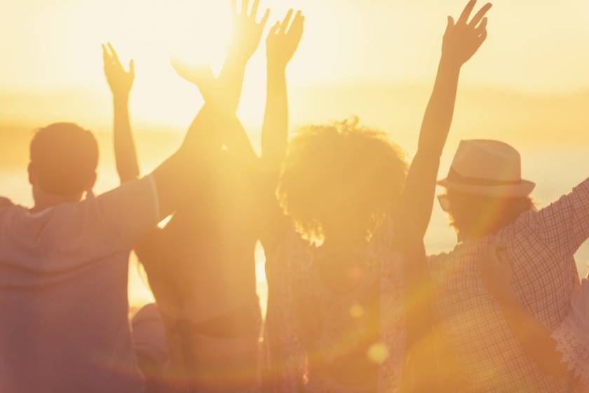 four friends with uplifted arms at an outdoor concert - heavy sunshine making images mostly yellow